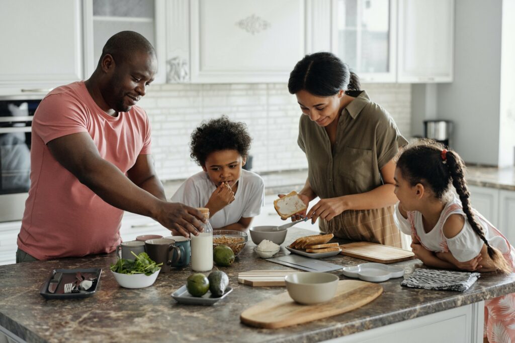 A family consisting of a mom, dad, son, and daughter gather around a countertop, seemingly preparing a meal together