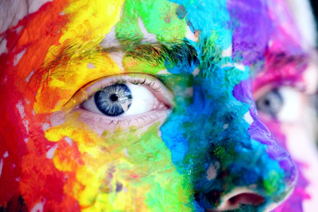 A close-up image of a person with rainbow stripes painted vertically on their face