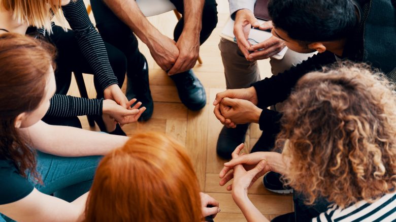 A group of people sit in a circle, seemingly participating in a support group.